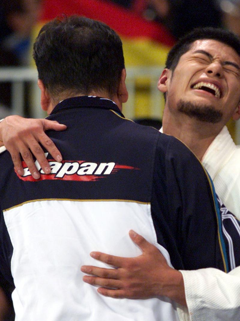 male judoka Satoshi Fujimoto hugs another man