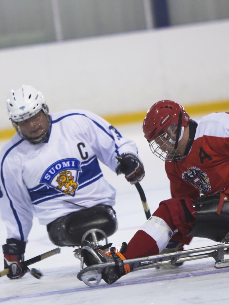 male Para ice hockey player Markku Hirvela defends the puck from a Polish player