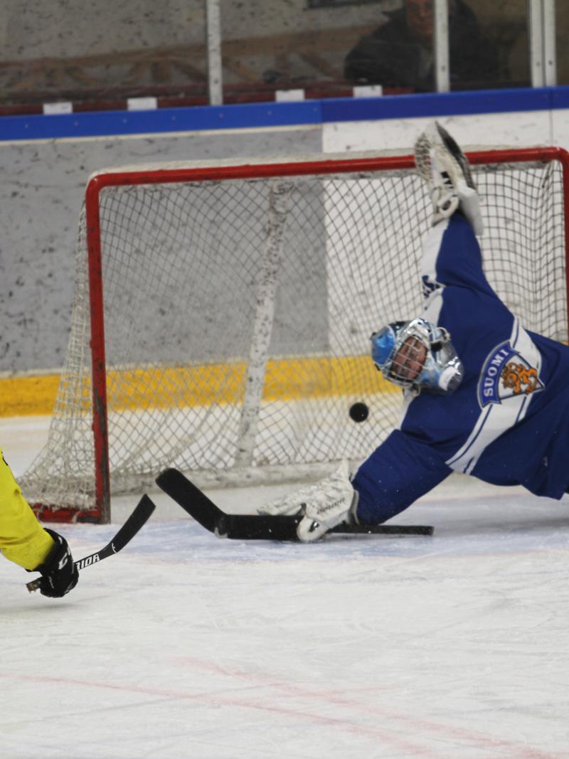 A man on sledge hockey scoring a goal against a goalkeeper trying to defend the puck
