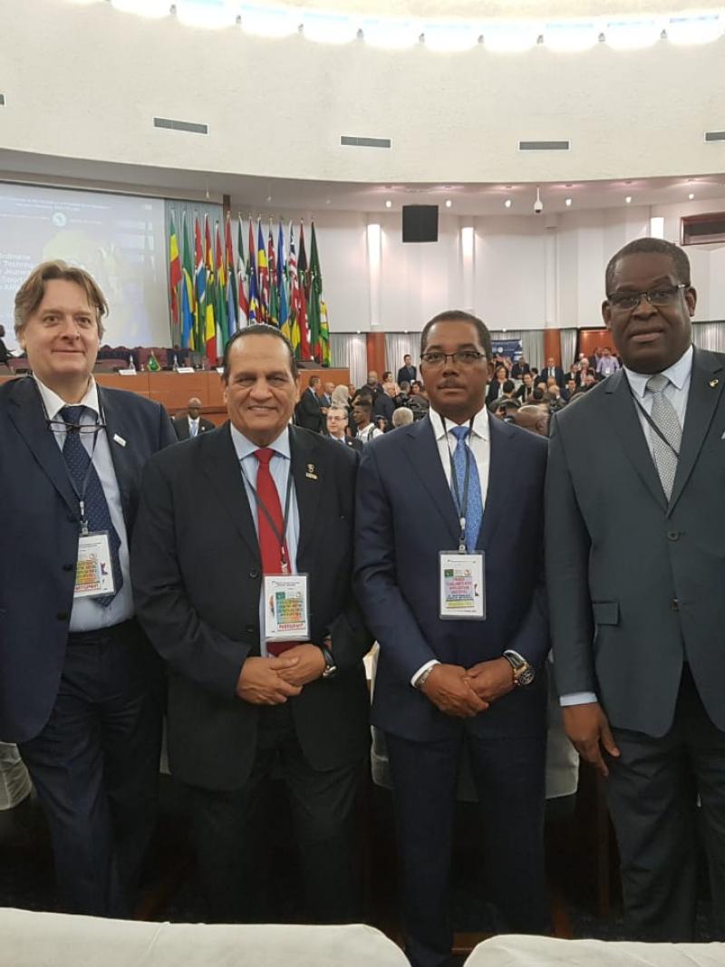 four men including Leonel da Rocha Pinto standing in suits in a conference hall