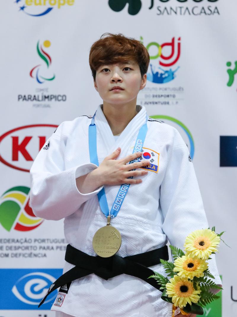 female judoka Soohee Choi holds her hand over her heart on the podium with a gold medal round her neck
