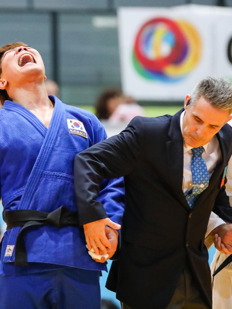A men in suit holding the hands of two men in judo kimonos