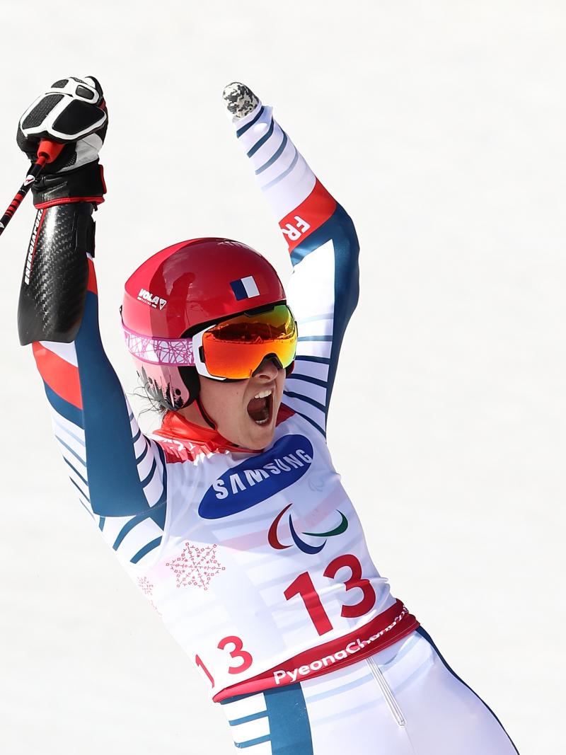female Para alpine skier Marie Bochet raises her arms on the slopes after crossing the finish line