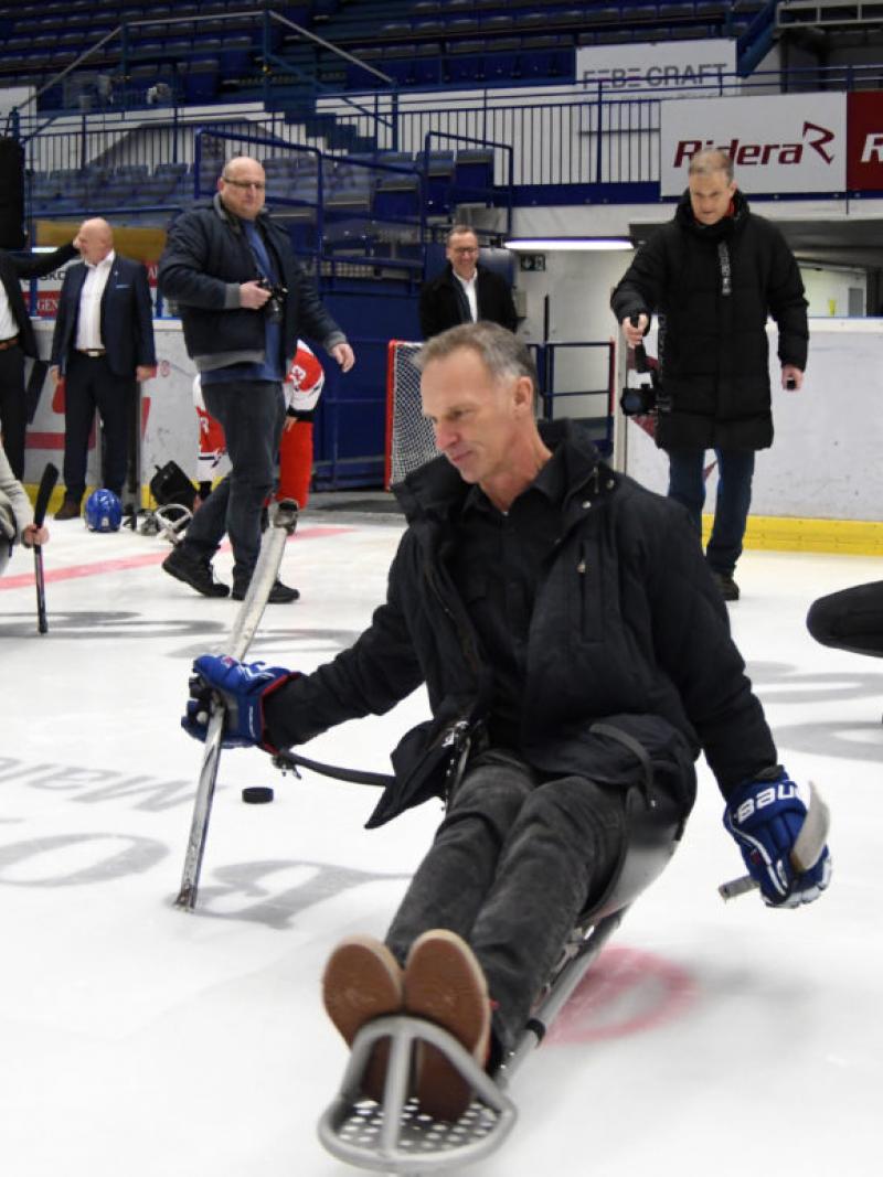A group of people on an ice rink with a man trying Para ice hockey