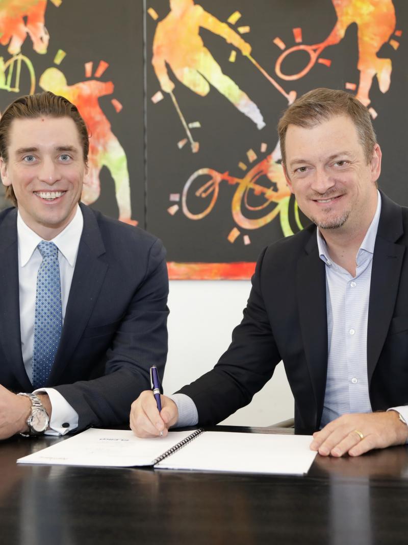 Two men smiling while one of the signs a contract