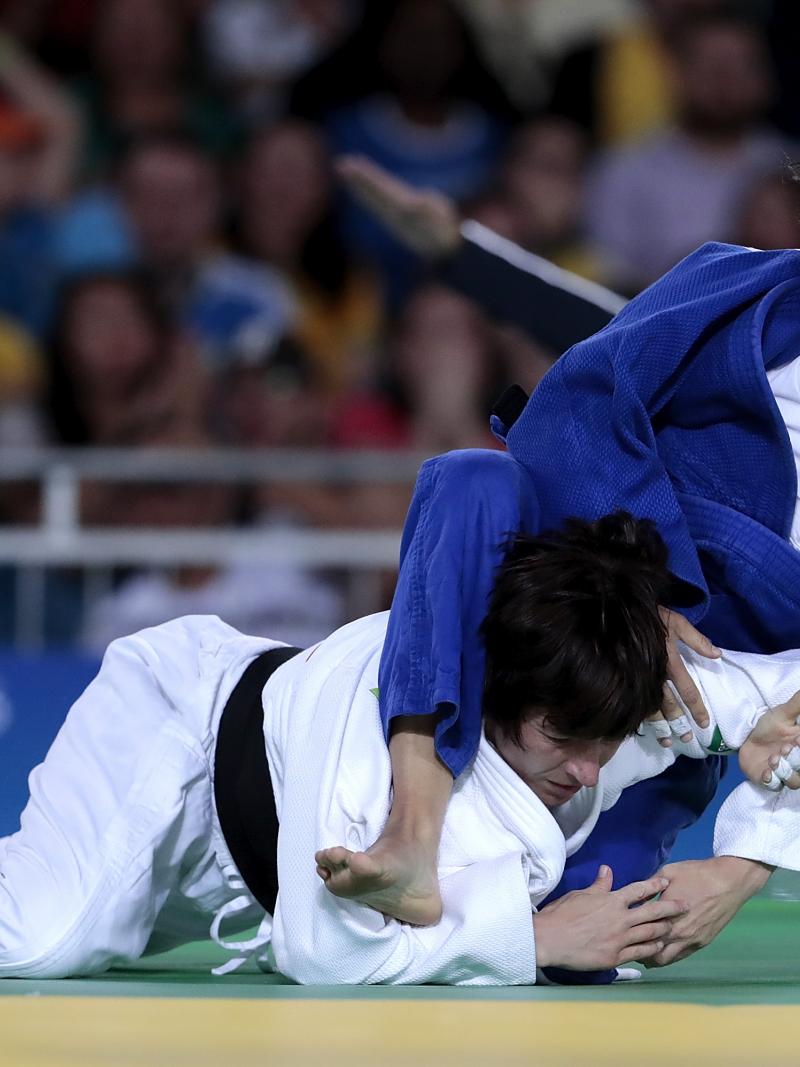 Female judoka Sandrine Martinet in a blue robe throws a judoka in a white robe onto the mat