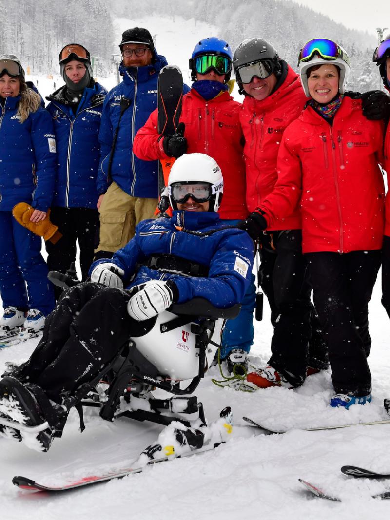 a group of skiing technical people standing behind a male Para alpine sit skier on the ski slope