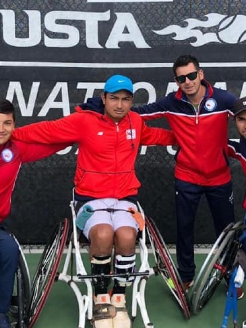 three male wheelchair tennis players and another man with their arms around eachother on a hard court