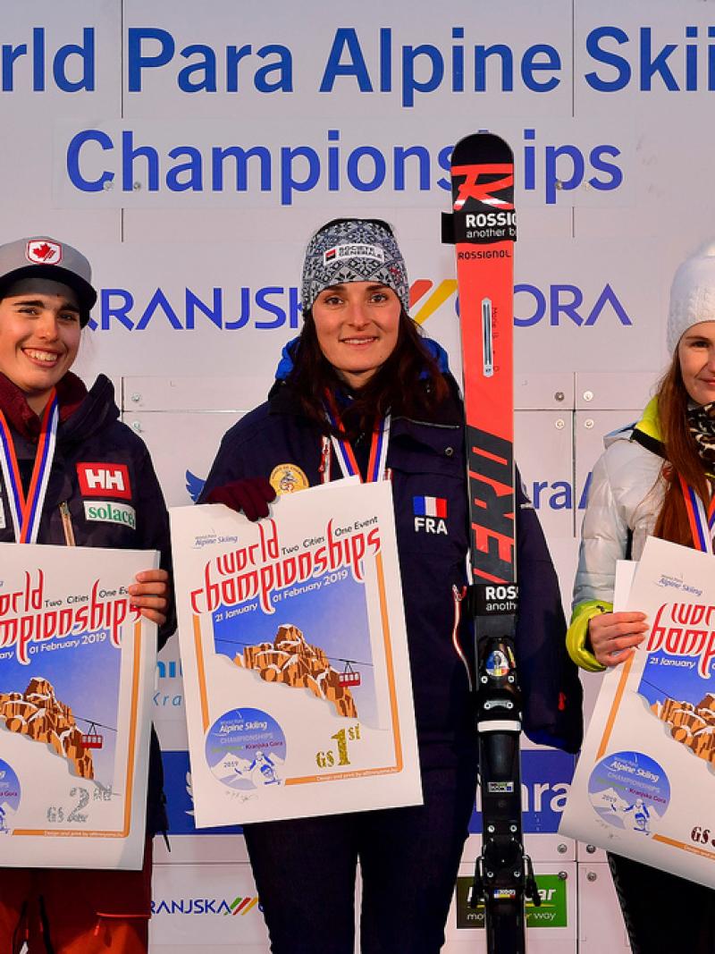 three female skiers including Marie Bochet standing on the podium holding prints
