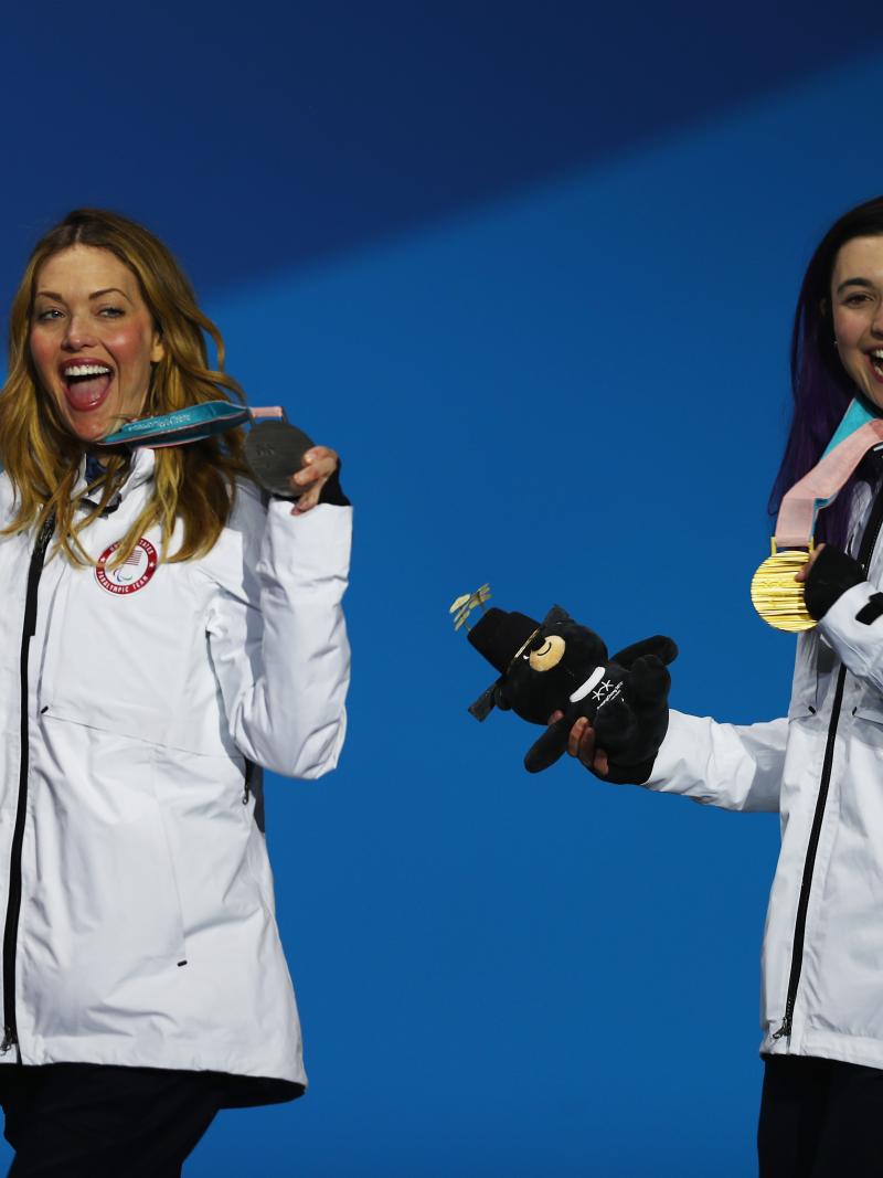 female Para snowboarders Amy Purdy and Brenna Huckaby holding up their medals and waving 