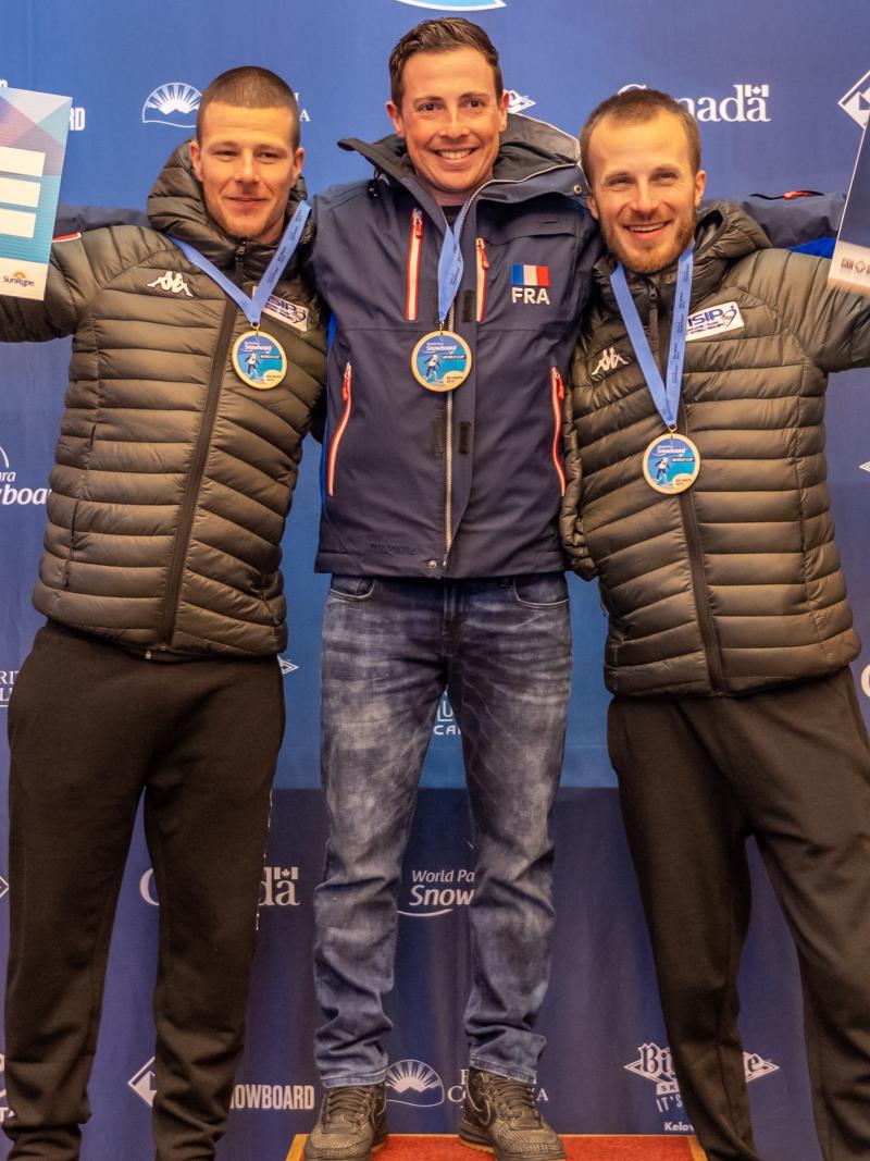 three male Para snowboarders with Maxime Montaggioni in the middle standing on the podium with their arms around eachother