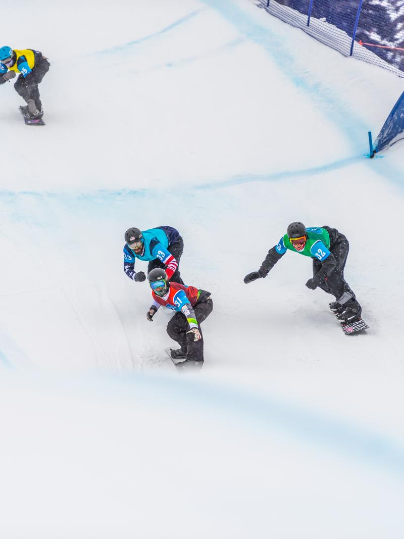 four male Para snowboarders racing on the snow with Alex Massie on the right