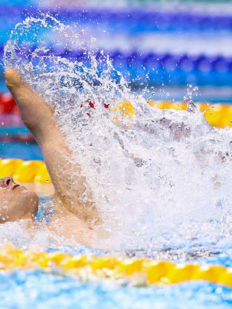 male Para swimmer Cameron Leslie lifts his arm up out of the water during a backstroke race