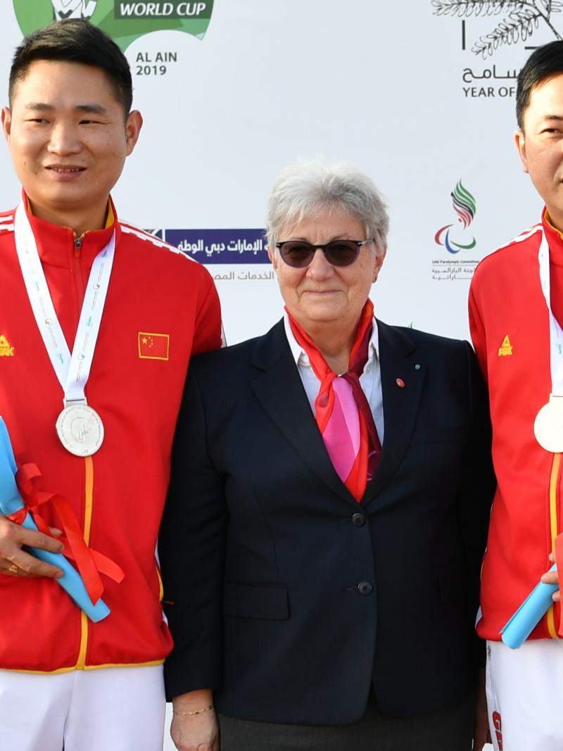 Chinese Para shooters Yang Chao and Huang Xing standing either side of a woman and smiling on the podium