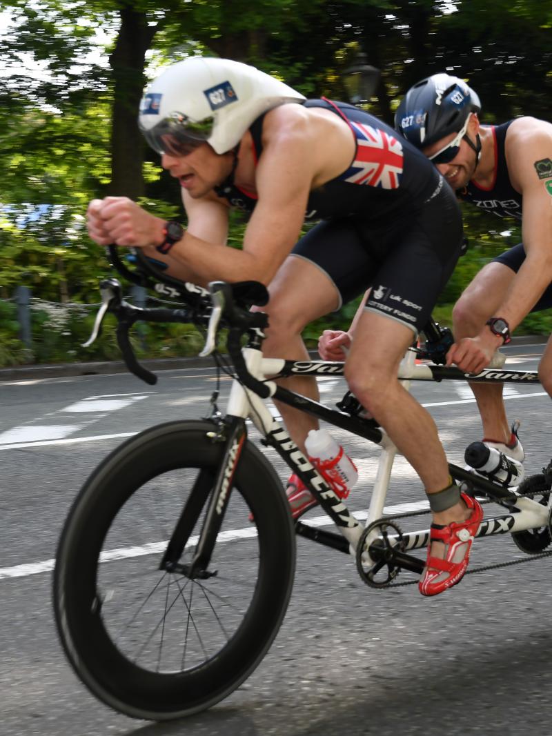 male Para triathlete Dave Ellis cycling on a tandem bike behind his guide