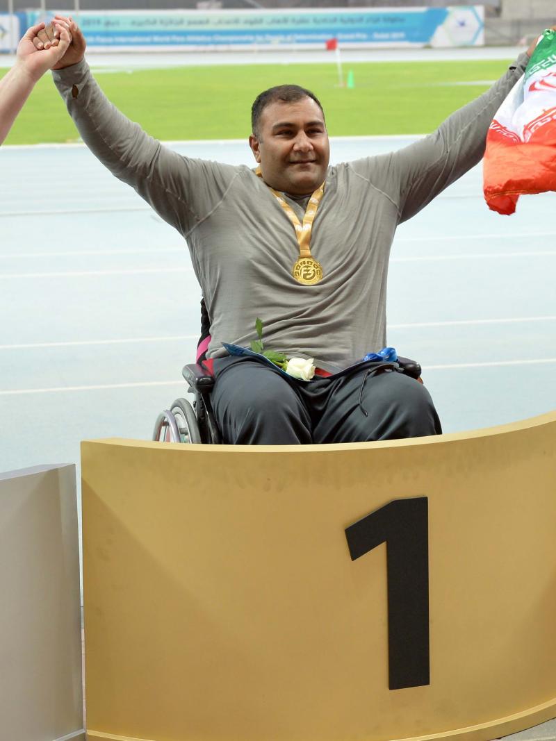three male Para athletes in wheelchairs on the podium with Hamed Amiri in the centre holding an Iranian flag