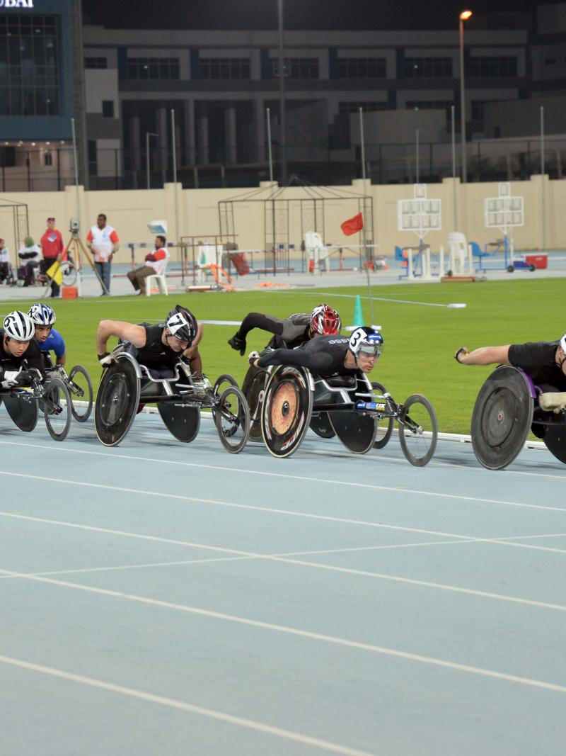 Group of men in racing chairs compete on a track