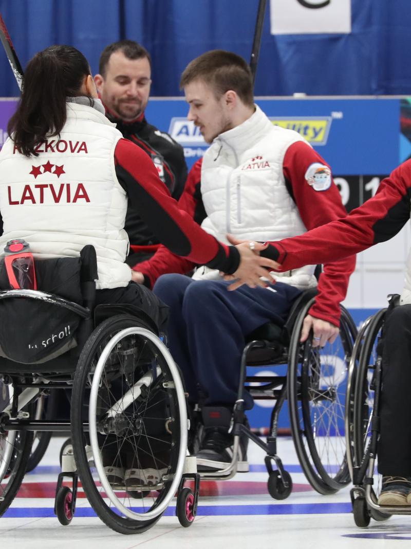 wheelchair curlers from Latvia high-five after beating Canada on the ice