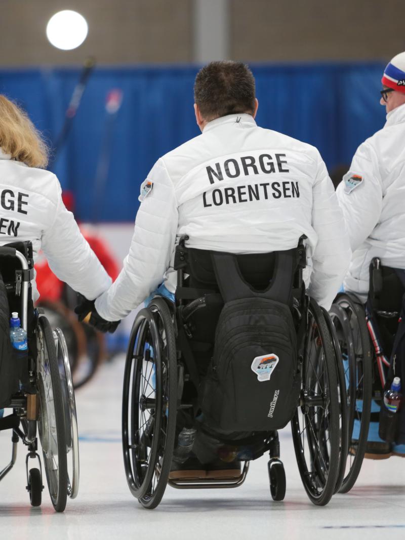 three wheelchair curlers with their backs to the camera with Norway on their jackets
