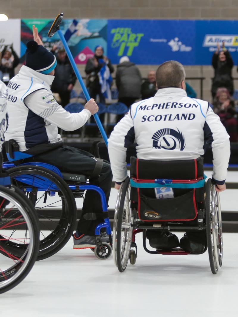 Four wheelchair curlers celebrating and waving to the crowd