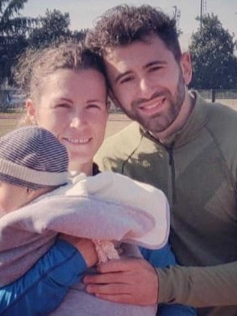 Female Para athlete Arjola Dedaj standing next to her male partner holding a baby boy