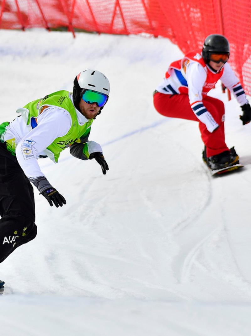 two male Para snowboarders racing down the slope head to head