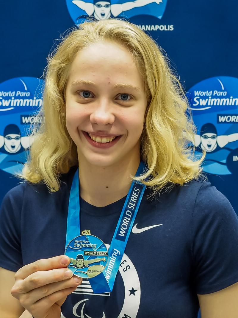 female Para swimmer Julia Gaffney smiles and holds up a gold medal