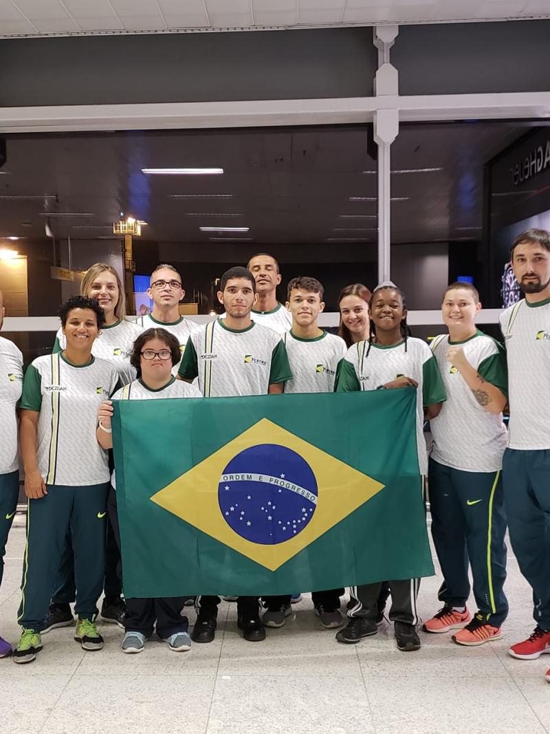 female Para taekwondo fighter Debora Menezes with other fighters holding a Brazilian flag