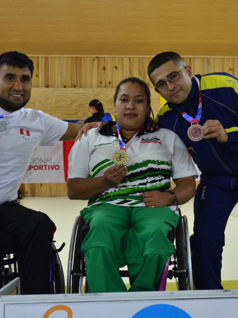 female Para shooter Maria Teresa Restrepo sitting a wheelchair with a male athlete either side holding up medals