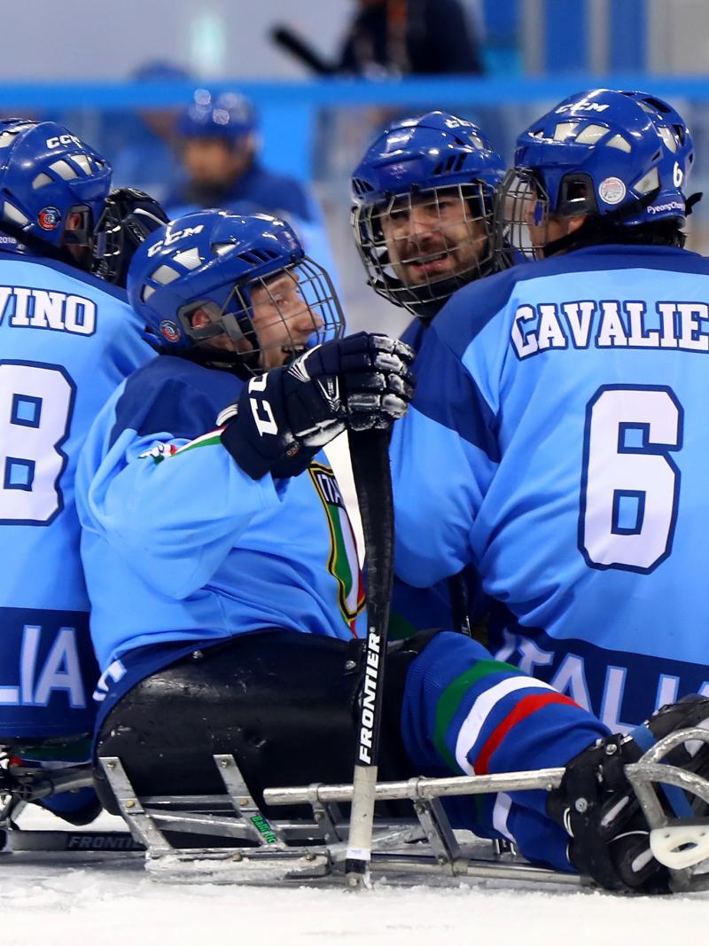 male Para ice hockey player Nils Larchi being hugged on the ice by his teammates