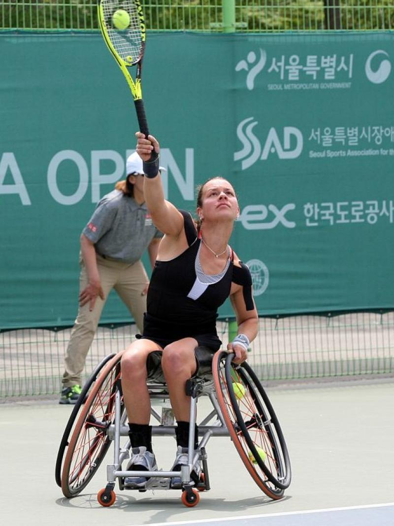 female wheelchair tennis player Marjolein Buis hits an overhead forehand on a hard court