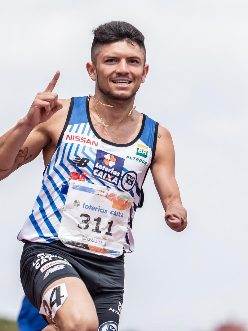 male Para athlete Petrucio Ferreira raises his finger as he crosses the finish line 