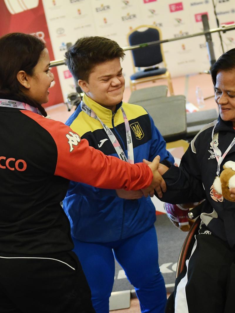 three female powerlifters shaking hands together on the podium