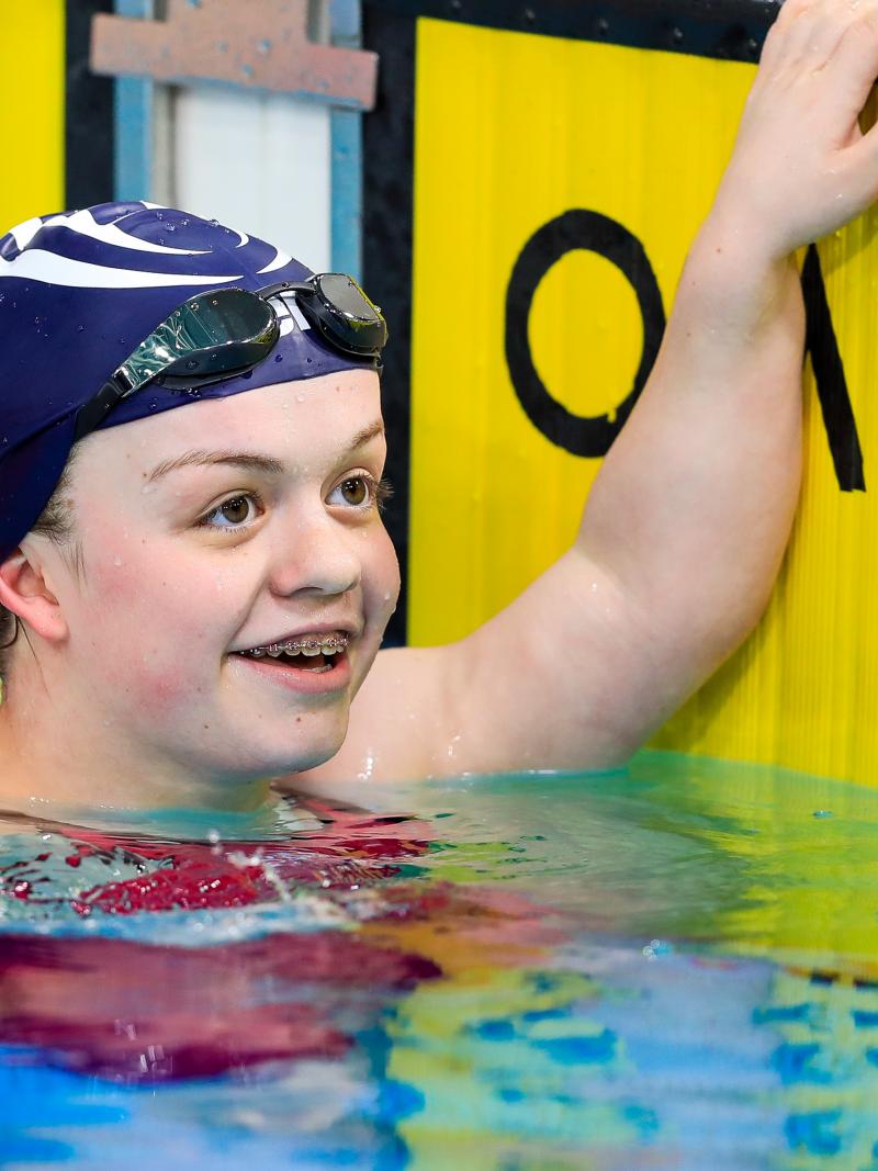female Para swimmer Maisie Summers-Newton holds onto the wall and smiles in the pool at the end of the race