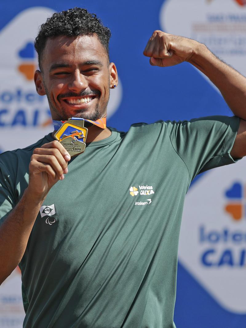 male Para athlete Daniel Martins holds up his arm and fist pumps while holding a gold medal and smiling