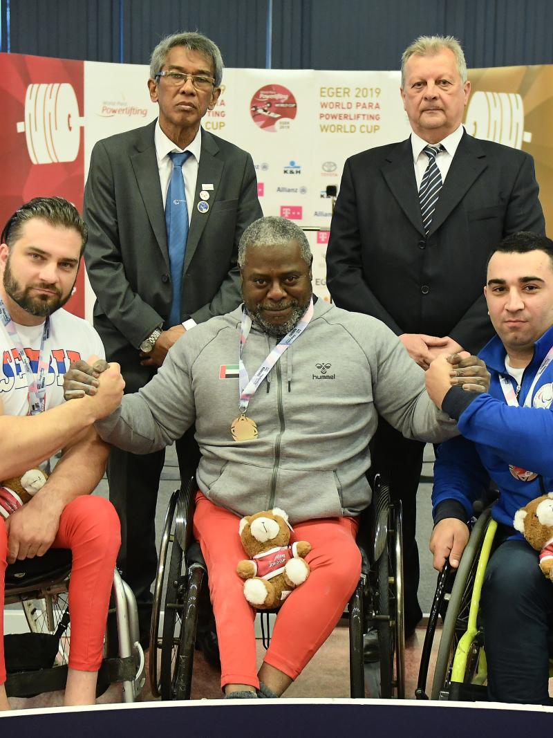 male Para powerlifter Mohammed Khamis Khalaf in the middle of two other powerlifters on the podium with their arms around eachother 
