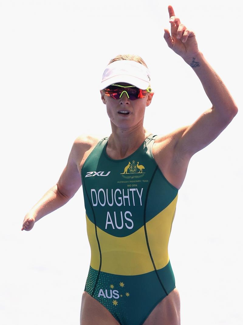 female Para triathlete Kate Doughty raises her hand and points to the sky as she crosses the finish line