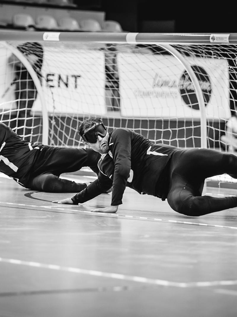 a team of male goalball players standing with their arms linked on a court
