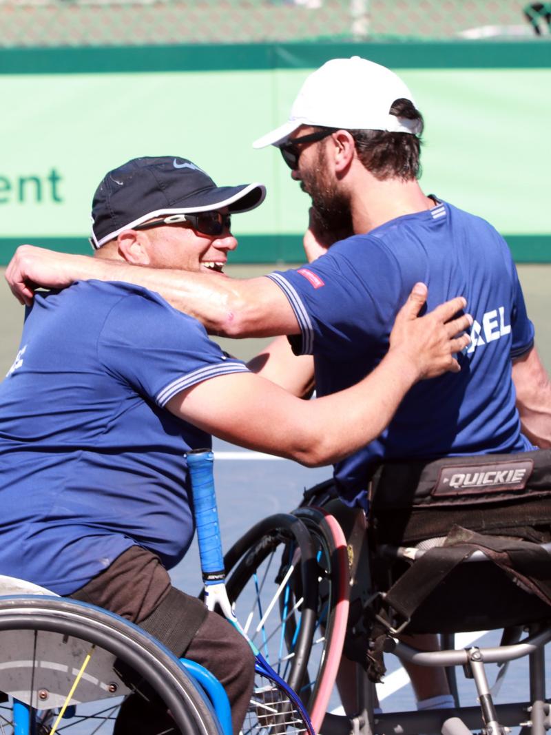 two male wheelchair tennis players from Israel hug on a hard court 