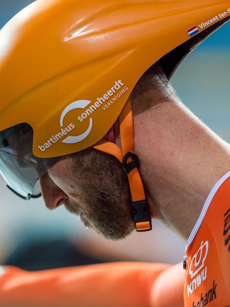 Dutch cyclist Vincent Ter Schure looking down while wearing a competition helmet and orange gear