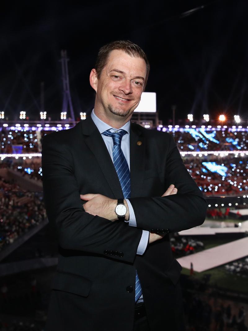 IPC President Andrew Parsons smiles and crosses arms with the PyeongChang 2018 stadium in the background during the Closing Ceremony