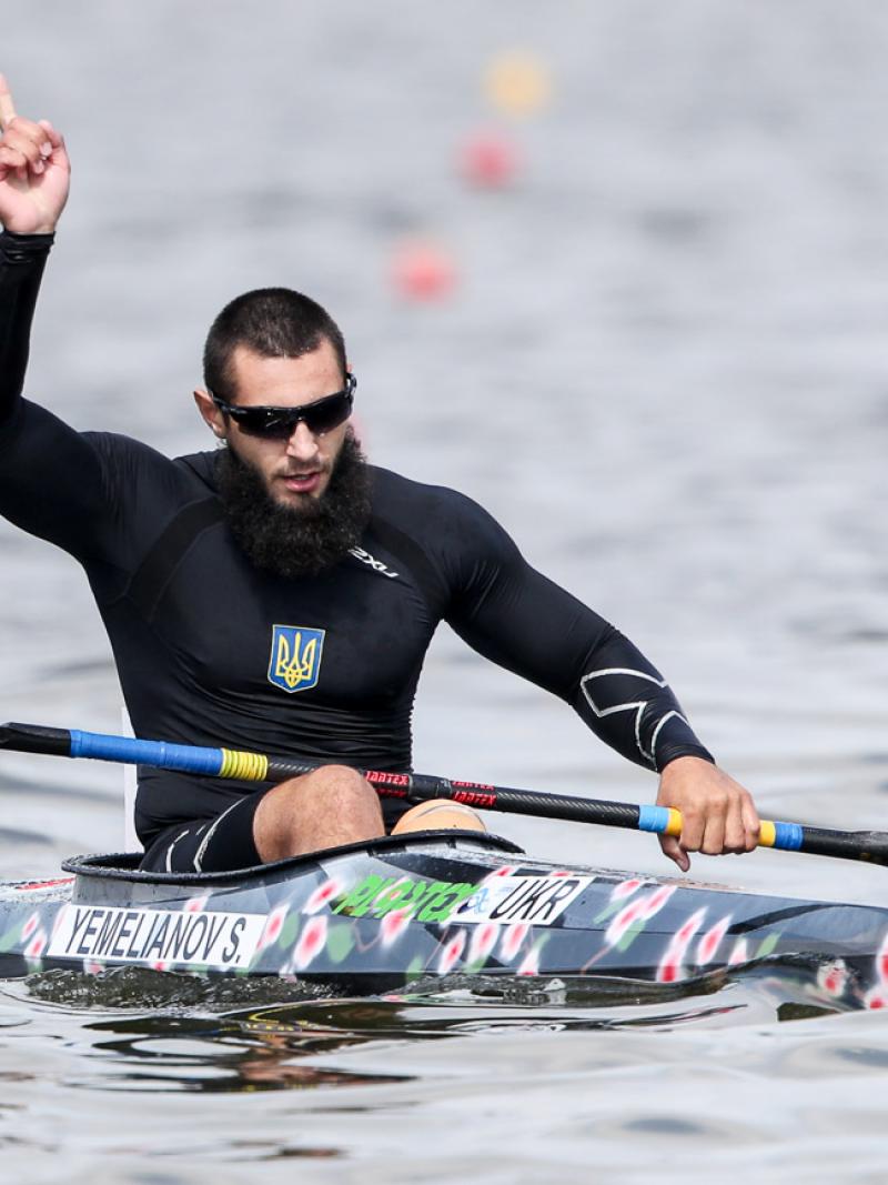 Serhii Yemelianov celebrates in the canoe with his hand in the air after winning gold