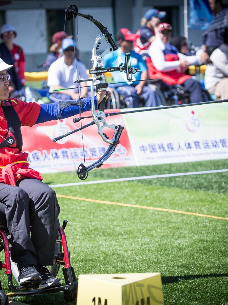 Chiense female archer in a wheelchair pulls back on her bow string