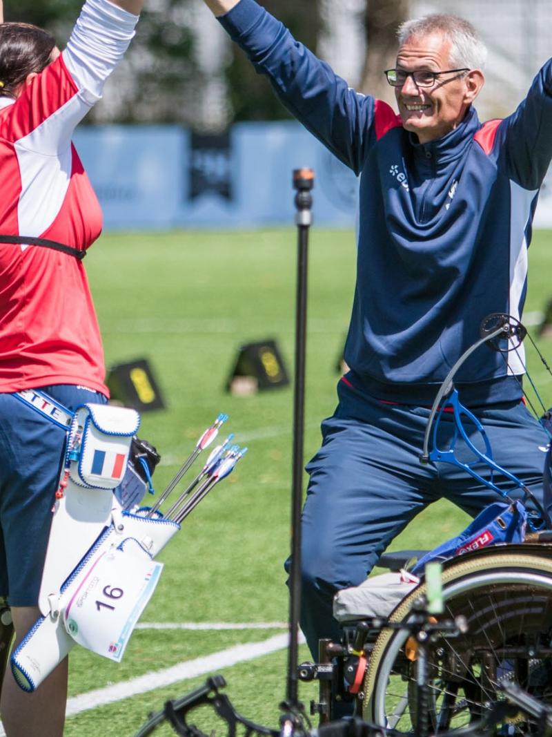 female Para archer Julie Chupin raises her arms in celebration with her coach