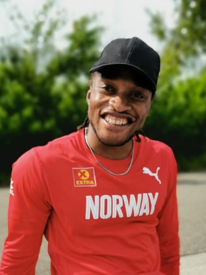 A man with a shirt a long-sleeved red shirt written Norway seated on the sidewalk