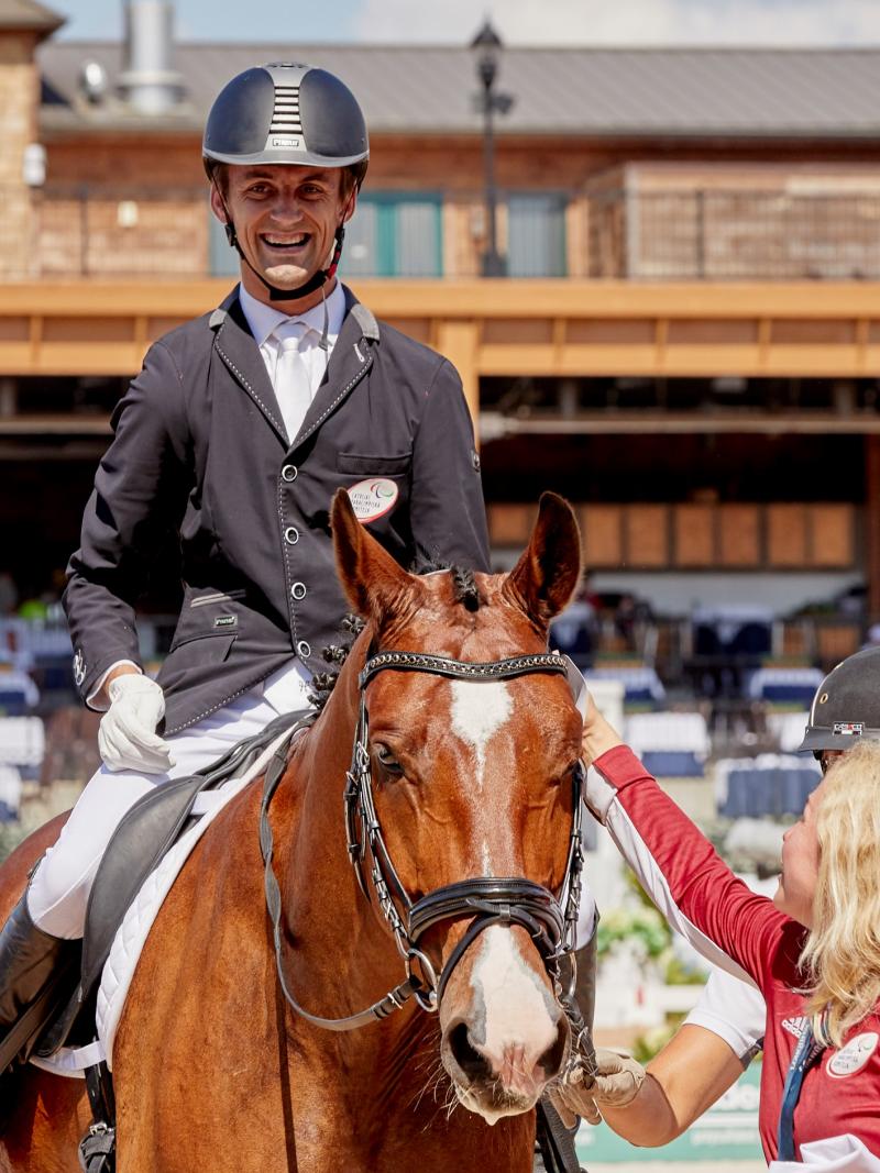 Latvian male dressage rider with celebral palsy smiles on a horse