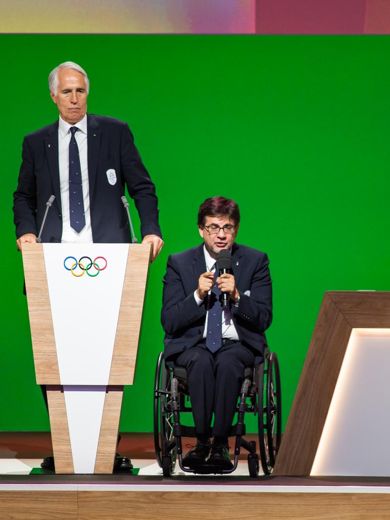 A man standing and another man in a wheelchair on stage