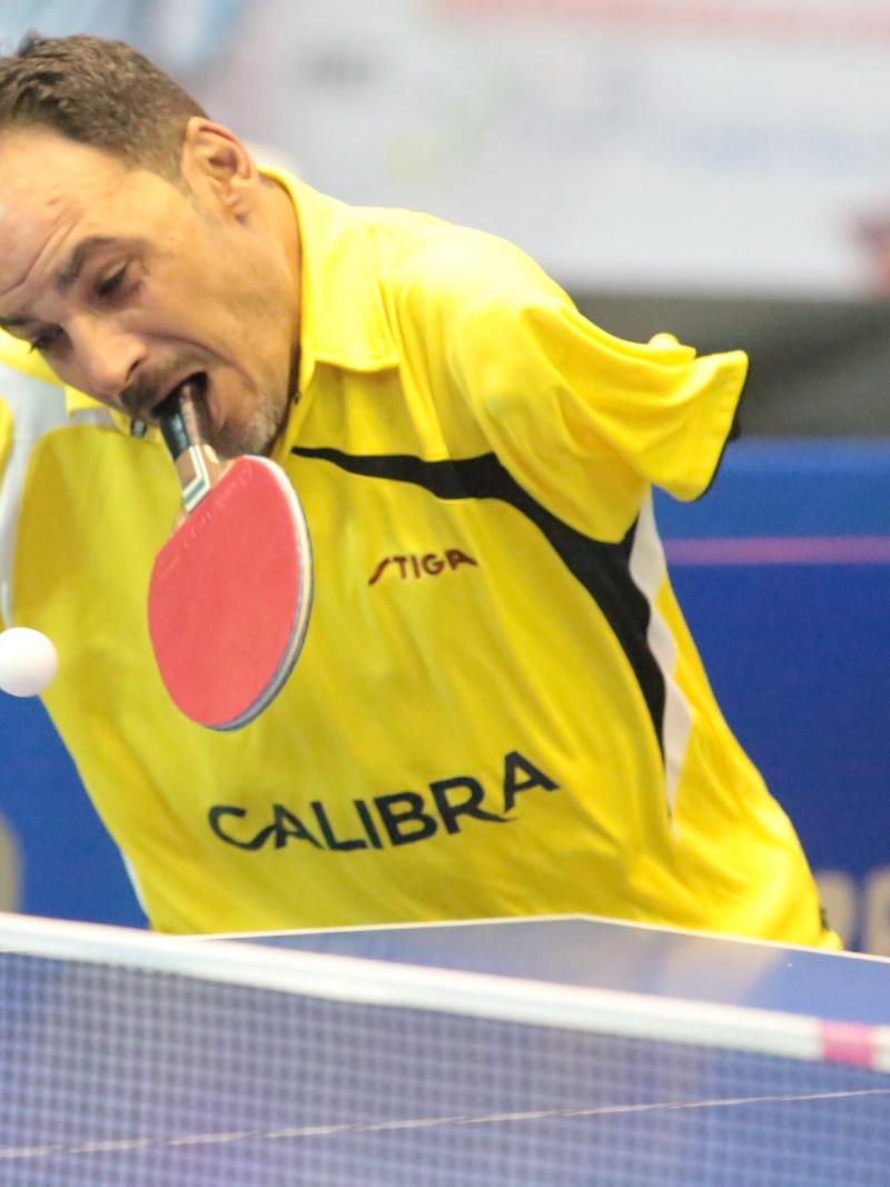 Egyptian male table tennis player holds racket in mouth and attempts to hit the ball