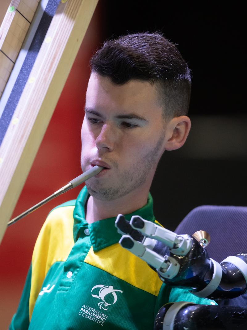 Australian male boccia player holds device in mouth to push ball down ramp
