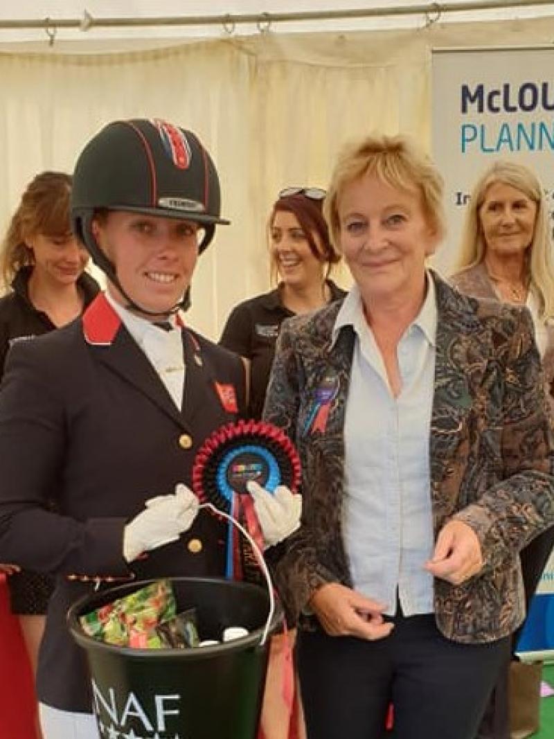 British female dressage athlete holds bucket of prize with an organiser